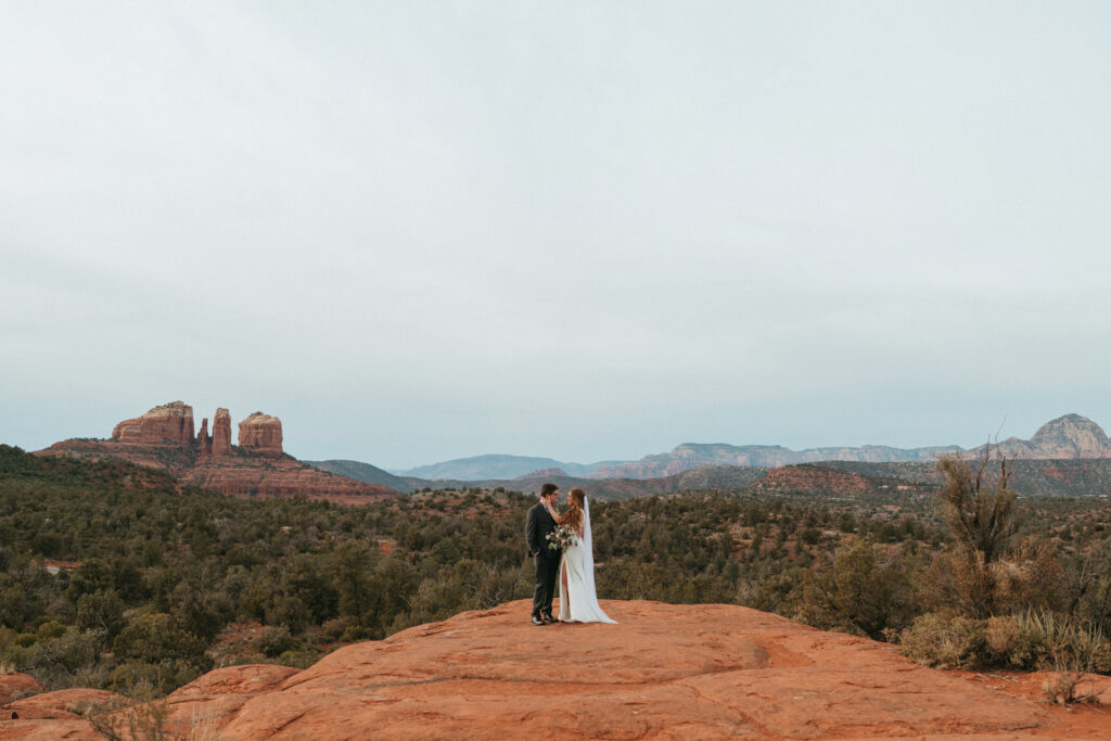 Wide landscape view of a couple standing on red rocks for their Sedona micro wedding photography.